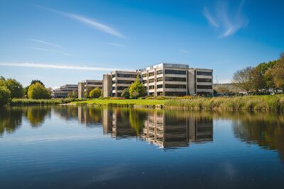An office building on a sunny day, the building is next to a lake and you can see the building reflected in the lake