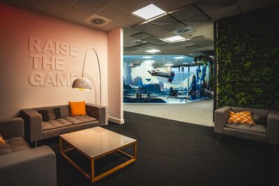 A room with three grey sofas, orange cushions, a large lamp and a white wall with 3d letters reading 